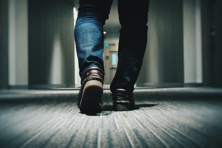 A close up view of a man in jeans and brown loafers walking down an office hallway.